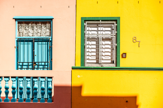 View of vibrant pink and yellow facades of traditional houses with colorful window frames and security bars in the Bo Kaap neighborhood Cape Town Western Cape South Africa. View of vibrant pink and yellow facades of traditional houses with colorful window frames and security bars in the Bo Kaap neighborhood Cape Town Western Cape South Africa.