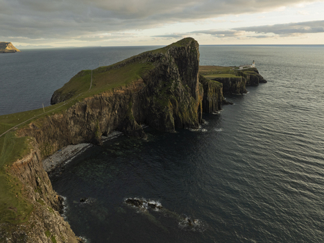 Aerial view of Neist Point Lighthouse perched on dramatic cliffs overlooking the sea at sunset with golden light hitting the rugged coastline of Scotland United Kingdom. Aerial view of Neist Point Lighthouse perched on dramatic cliffs overlooking the sea at sunset with golden light hitting the rugged coastline of Scotland United Kingdom.