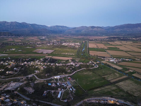 Aerial view of the rural landscape surrounding Saranda with agricultural fields winding roads and distant mountains under a soft evening sky in Saranda Vlore County Albania. Aerial view of the rural landscape surrounding Saranda with agricultural fields winding roads and distant mountains under a soft evening sky in Saranda Vlore County Albania.