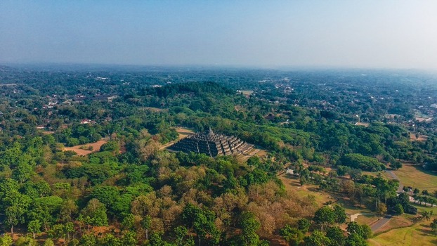Aerial view of Borobudur Temple surrounded by lush green forest and trees in the countryside in Kecamatan Borobudur Jawa Tengah Indonesia.