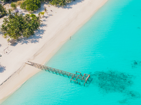 Aerial view of turquoise waters gently embracing the white sandy shores near a long wooden pier stretching into the sea Vashafaru Island Maldives.