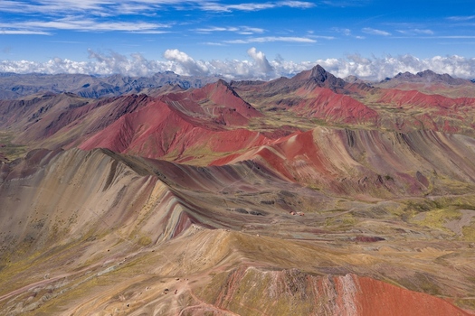 Aerial view of Vinicunca Rainbow Mountain featuring vibrant multi colored mineral layers rugged Andean peaks and scattered clouds under a bright blue sky in Cusco Cuzco Peru. Aerial view of Vinicunca Rainbow Mountain featuring vibrant multi colored mineral layers rugged Andean peaks and scattered clouds under a bright blue sky in Cusco Cuzco Peru.