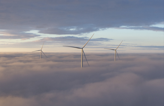 Aerial view of three wind turbines rising above a thick blanket of clouds under a soft pastel sky at dawn Netherlands. Aerial view of three wind turbines rising above a thick blanket of clouds under a soft pastel sky at dawn Netherlands.