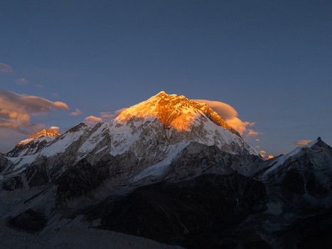 Aerial view of Mount Everest illuminated by golden hour sunlight with snow capped peaks and dramatic clouds in the Himalayas Nepal.