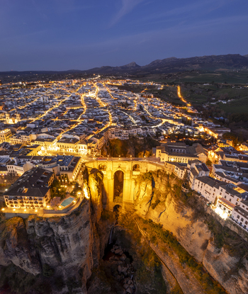 Aerial view of the illuminated Puente Nuevo bridge spanning the deep El Tajo gorge in the historic town of Ronda with glowing streetlights in Ronda Andalusia Spain. Aerial view of the illuminated Puente Nuevo bridge spanning the deep El Tajo gorge in the historic town of Ronda with glowing streetlights in Ronda Andalusia Spain.