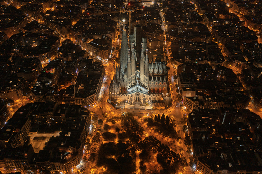 Aerial view of the illuminated Sagrada Familia at night surrounded by the dense urban grid and glowing streetlights of the city in Barcelona Catalonia Spain. Aerial view of the illuminated Sagrada Familia at night surrounded by the dense urban grid and glowing streetlights of the city in Barcelona Catalonia Spain.