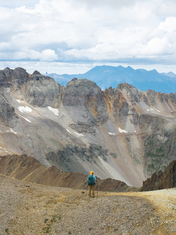 Aerial view of a hiker with a backpack and trekking poles standing on a rocky ridge overlooking Yankee Boy Basin and Mount Sneffels in the San Juan Mountains Ouray Colorado United States. Aerial view of a hiker with a backpack and trekking poles standing on a rocky ridge overlooking Yankee Boy Basin and Mount Sneffels in the San Juan Mountains Ouray Colorado United States.