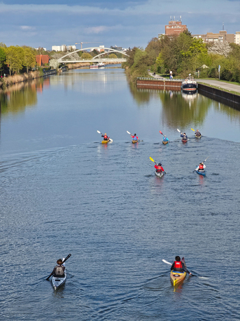 Hannover Germany 14 April 2026 View of a group of kayakers paddling along the calm waters of the Mittellandkanal surrounded by lush green trees and a modern bridge in the background.