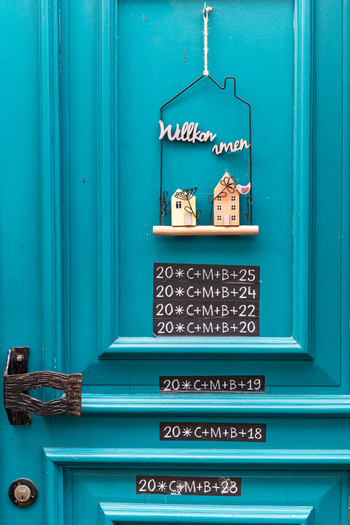 View of a bright turquoise wooden door featuring a decorative welcome sign and traditional chalk inscriptions in Monreal Rhineland Palatinate Germany. View of a bright turquoise wooden door featuring a decorative welcome sign and traditional chalk inscriptions in Monreal Rhineland Palatinate Germany.