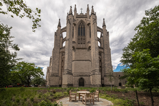 Washington District of Columbia United States 06 May 2025 View of Washington National Cathedral with gothic stone architecture towering spires and a wooden table set in the garden under a cloudy sky.
