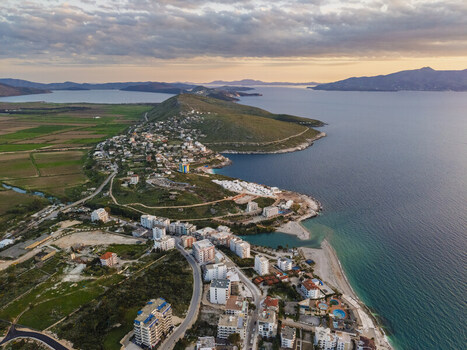 Aerial view of Saranda coastal town with modern buildings winding roads and green hills overlooking the Ionian Sea in Saranda Vlore County Albania. Aerial view of Saranda coastal town with modern buildings winding roads and green hills overlooking the Ionian Sea in Saranda Vlore County Albania.