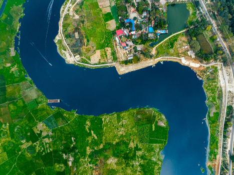 Aerial view of a winding river flowing through lush green agricultural fields and rural settlements with small boats on the water near Dhaka Dhaka Division Bangladesh. Aerial view of a winding river flowing through lush green agricultural fields and rural settlements with small boats on the water near Dhaka Dhaka Division Bangladesh.