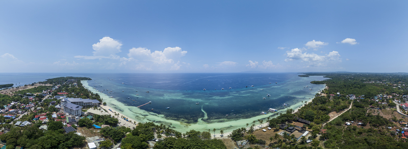 Aerial view of Doljo beach featuring turquoise waters small boats a coastal resort and lush tropical vegetation Panglao Central Visayas Philippines.
