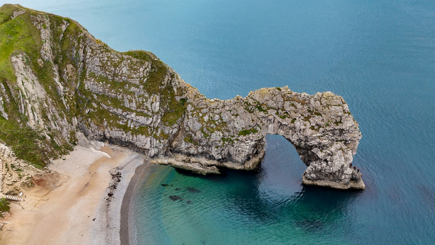 Aerial view of Durdle Door a natural limestone arch on the Jurassic Coast with rugged cliffs sandy beach and deep blue sea in Wareham England United Kingdom. Aerial view of Durdle Door a natural limestone arch on the Jurassic Coast with rugged cliffs sandy beach and deep blue sea in Wareham England United Kingdom.