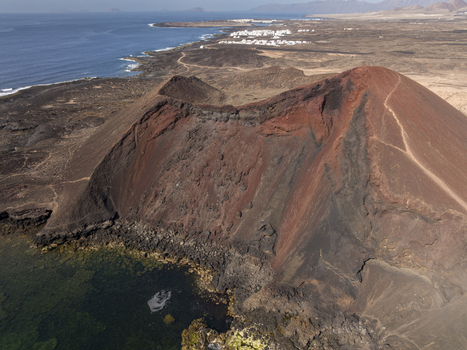 Aerial view of the volcanic crater in Lanzarote featuring rugged red and black slopes rocky terrain and the surrounding coastline in Lanzarote Canarias Spain. Aerial view of the volcanic crater in Lanzarote featuring rugged red and black slopes rocky terrain and the surrounding coastline in Lanzarote Canarias Spain.