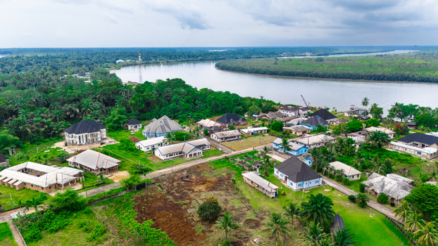 Aerial view of a residential settlement nestled along a riverbank featuring scattered houses lush green vegetation and palm trees in Minima Rivers Nigeria.