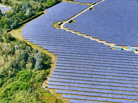 Aerial view of a large solar panel farm with rows of blue photovoltaic modules surrounded by lush green trees and vegetation in Torrazza Piemonte Piemonte Italy. Aerial view of a large solar panel farm with rows of blue photovoltaic modules surrounded by lush green trees and vegetation in Torrazza Piemonte Piemonte Italy.