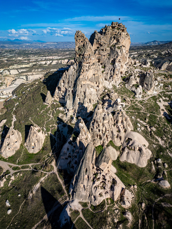 Aerial view of the historic Uchisar Castle carved into volcanic rock formations surrounded by winding paths and the rugged landscape of Cappadocia in Uchisar Nevsehir Turkiye. Aerial view of the historic Uchisar Castle carved into volcanic rock formations surrounded by winding paths and the rugged landscape of Cappadocia in Uchisar Nevsehir Turkiye.