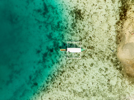 Aerial view of a traditional outrigger boat floating in the clear turquoise waters of Bucas Grande near the sandy coastline of Siargao Philippines. Aerial view of a traditional outrigger boat floating in the clear turquoise waters of Bucas Grande near the sandy coastline of Siargao Philippines.