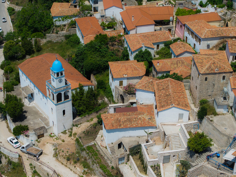 Aerial view of traditional houses with red tiled roofs and a white church with a blue dome in Dhermi Vlore County Albania. Aerial view of traditional houses with red tiled roofs and a white church with a blue dome in Dhermi Vlore County Albania.