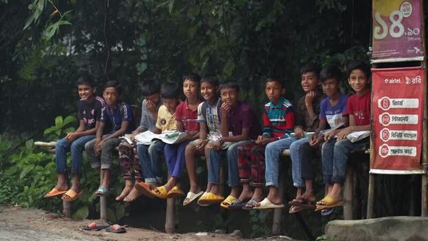 View of a group of smiling boys sitting outdoors Bangladesh.