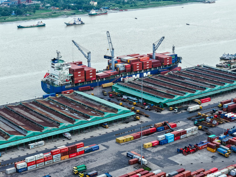 Aerial view of Chattogram Port with a large container ship docked at the pier surrounded by colorful shipping containers and warehouse buildings in Chittagong Chittagong Division Bangladesh.