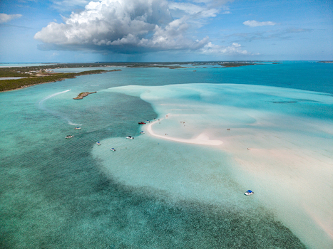 Aerial view of Man O War Cay Sandbar with small boats anchored in turquoise water and people walking on the white sand under large clouds in Rolletown Exuma The Bahamas. Aerial view of Man O War Cay Sandbar with small boats anchored in turquoise water and people walking on the white sand under large clouds in Rolletown Exuma The Bahamas.