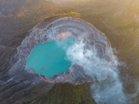 Aerial view of the turquoise acidic crater lake of Ijen volcano with sulfurous smoke rising from the rugged volcanic rim in Ijen East Java Indonesia.