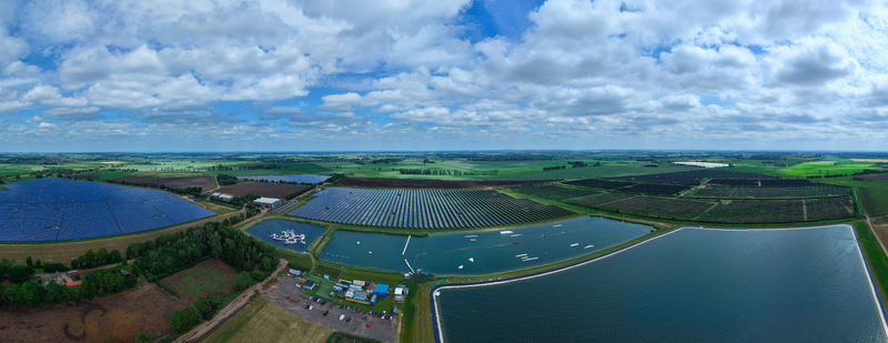 Aerial view of Fenland Aqua Park featuring inflatable obstacles on a lake next to a large solar farm under a cloudy sky in Whittlesey England United Kingdom.