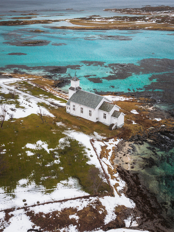 Aerial view of a white church standing out against the contrasting turquoise waters and snow covered ground Gimsøysand Nordland Norway. Aerial view of a white church standing out against the contrasting turquoise waters and snow covered ground Gimsøysand Nordland Norway.