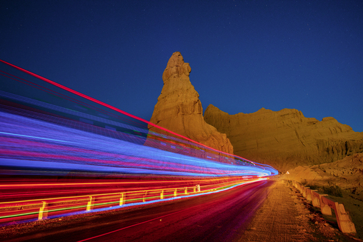 View of the Makran Coastal Highway at night with vibrant light trails set against the Princess of Hope rock formation under a clear starry sky in Balochistan Pakistan.