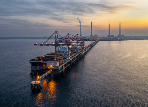 Aerial view of Orot Rabin Power Plant with a large cargo ship docked at the pier industrial cranes and smoking chimneys under a sunset sky in Hadera Haifa District Israel. Aerial view of Orot Rabin Power Plant with a large cargo ship docked at the pier industrial cranes and smoking chimneys under a sunset sky in Hadera Haifa District Israel.