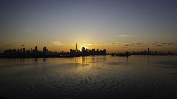 Aerial view of the New York skyline at sunset with the sun glowing behind skyscrapers and reflecting on the calm waters of the Hudson River New York New York United States.