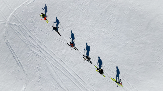 Aerial view of a group of skiers ascending a snowy slope near Pointe Percee with long shadows and tracks on the white snow Le Reposoir Auvergne Rhone Alpes France. Aerial view of a group of skiers ascending a snowy slope near Pointe Percee with long shadows and tracks on the white snow Le Reposoir Auvergne Rhone Alpes France.