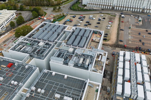Aerial view of a large data center facility featuring industrial rooftop cooling units and complex infrastructure situated near a parking lot in the United Kingdom.