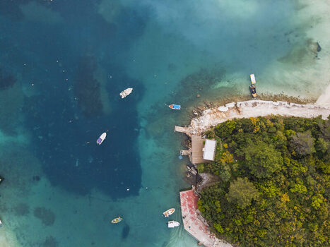 Aerial view of Ksamil coastline with small boats floating in turquoise water lush green vegetation and a wooden pier in Ksamil Vlore County Albania. Aerial view of Ksamil coastline with small boats floating in turquoise water lush green vegetation and a wooden pier in Ksamil Vlore County Albania.