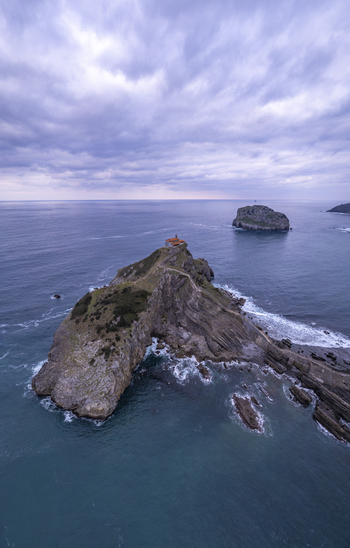 Aerial view of San Juan de Gaztelugatxe a historic hermitage on a rocky islet with a winding stone bridge surrounded by the Bay of Biscay in Gaztelugatxeko Doniene Euskadi Spain. Aerial view of San Juan de Gaztelugatxe a historic hermitage on a rocky islet with a winding stone bridge surrounded by the Bay of Biscay in Gaztelugatxeko Doniene Euskadi Spain.