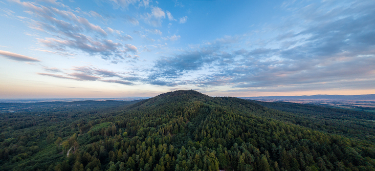 Aerial view of Radunia Mountain surrounded by dense evergreen forests and rolling hills under a vibrant sunset sky in Sobotka Lower Silesian Voivodeship Poland. Aerial view of Radunia Mountain surrounded by dense evergreen forests and rolling hills under a vibrant sunset sky in Sobotka Lower Silesian Voivodeship Poland.