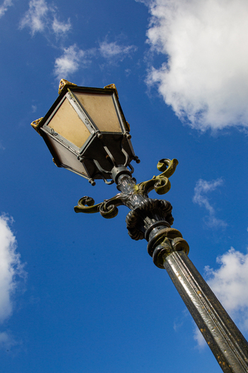 View of an ornate vintage street lamp with gold decorative elements against a bright blue sky with white clouds at Castle Groeneveld in Baarn Utrecht Netherlands.