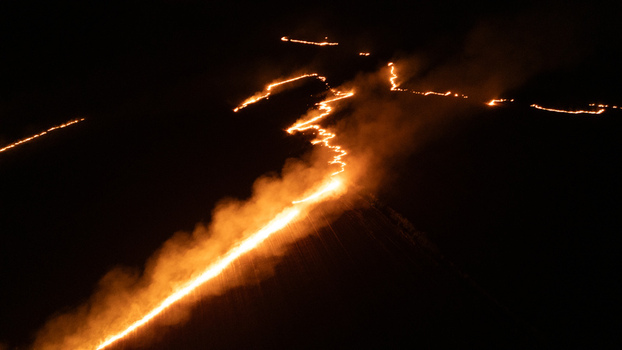 Aerial view of a fire line burning across the dark landscape at night with glowing embers and smoke trails visible in Sremska Mitrovica Vojvodina Serbia.