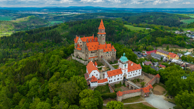Aerial view of Bouzov Castle with its iconic red tiled roofs and tall spire nestled among lush green forests and rolling hills Bouzov Olomoucky kraj Czechia. Aerial view of Bouzov Castle with its iconic red tiled roofs and tall spire nestled among lush green forests and rolling hills Bouzov Olomoucky kraj Czechia.