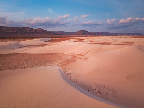 Aerial view of undulating dunes of white sand meet reddish plains under a vast blue sky revealing the stark beauty of the landscape Hamlah Socotra Yemen.
