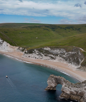 Aerial view of Durdle Door the iconic natural limestone arch on the Jurassic Coast with white cliffs sandy beach and a small boat in the blue sea in Wareham England United Kingdom. Aerial view of Durdle Door the iconic natural limestone arch on the Jurassic Coast with white cliffs sandy beach and a small boat in the blue sea in Wareham England United Kingdom.