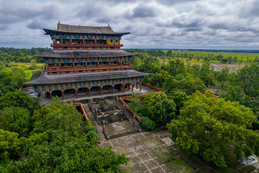 Aerial view of a multi tiered Buddhist monastery surrounded by lush greenery and fields in Nepal.
