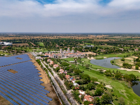 Ahmedabad Gujarat India 21 March 2026 Aerial view of Kalhaar Blues Greens Golf Club with lush fairways a pond and an adjacent solar panel farm under a clear sky.