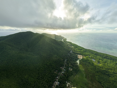 Aerial view of the lush green landscape meets the turquoise ocean under a sky streaked with sunlight and clouds Karimunjawa Central Java Indonesia.