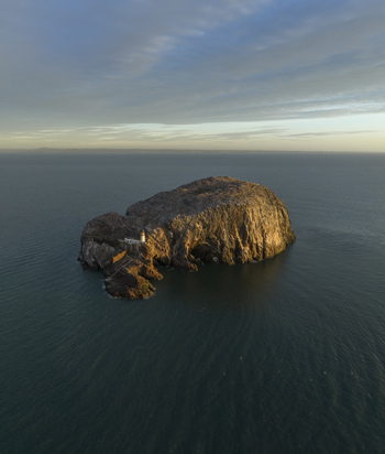 Aerial view of Bass Rock Lighthouse on the volcanic island of Bass Rock with steep cliffs and calm sea under soft golden light North Berwick Scotland United Kingdom. Aerial view of Bass Rock Lighthouse on the volcanic island of Bass Rock with steep cliffs and calm sea under soft golden light North Berwick Scotland United Kingdom.