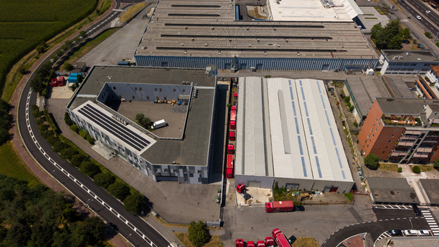 Aerial view of an industrial complex with large warehouse buildings rows of parked red trucks and paved loading areas situated in an urban setting in Milan Lombardy Italy. Aerial view of an industrial complex with large warehouse buildings rows of parked red trucks and paved loading areas situated in an urban setting in Milan Lombardy Italy.
