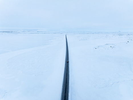Aerial view of a lonely road stretching through a vast snow covered landscape under a bright overcast sky in Egilsstadir Mulathing Iceland. Aerial view of a lonely road stretching through a vast snow covered landscape under a bright overcast sky in Egilsstadir Mulathing Iceland.
