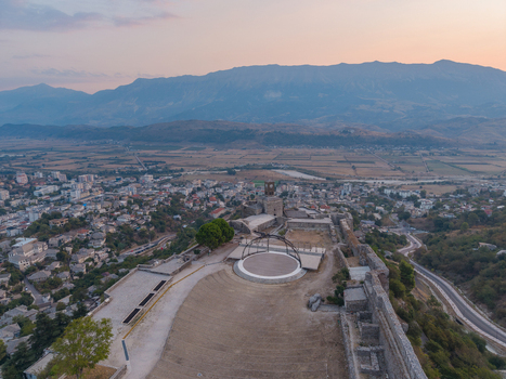 Aerial view of Gjirokaster Castle with historic stone walls open air stage and surrounding cityscape against mountains in Gjirokaster Gjirokaster County Albania. Aerial view of Gjirokaster Castle with historic stone walls open air stage and surrounding cityscape against mountains in Gjirokaster Gjirokaster County Albania.